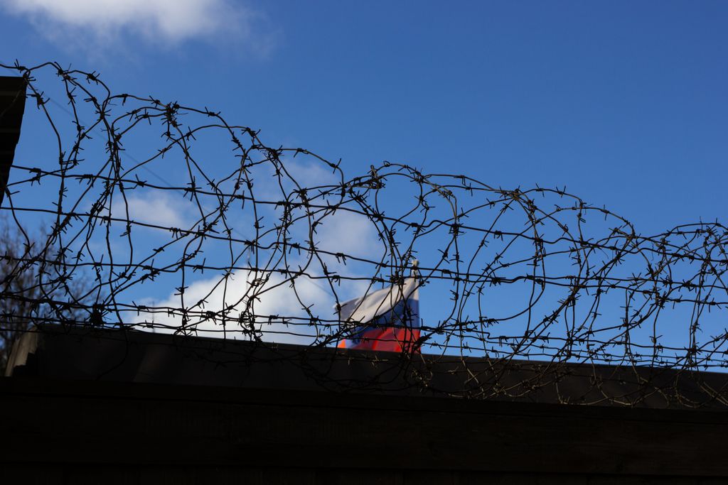 Silhouette of barbed wire with a flag in the background against a clear blue sky.