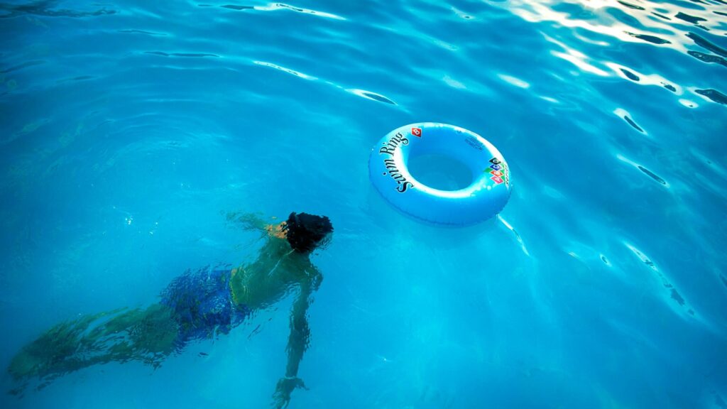 An individual swims underwater in a bright pool beside a floating swim ring.